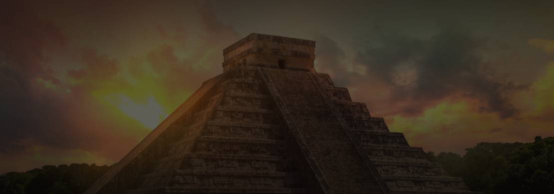 A photograph of an ancient Mesoamerican stone pyramid backlit by the setting sun