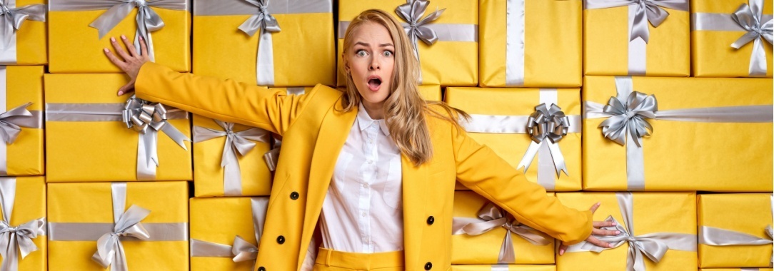 A photo of a woman in front of a wall of gifts with her arms outstretched looking overwhelmed by the choices.