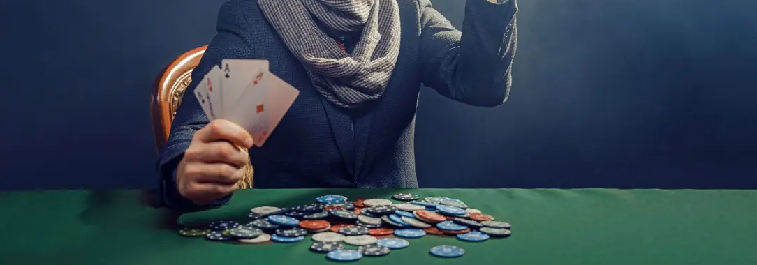 thirtyish man in suit with a scarf and a short beard holding four aces and smiling as if he doesn't believe his good luck