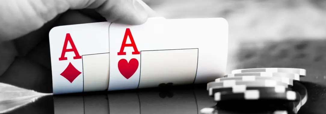 a black and white image of a poker table as a man half opens his cards to show a pair of red aces
