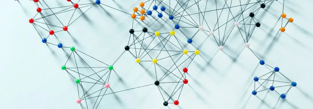 An image of a vibrant globe of colourful pushpins and threads on a light blue base, symbolizing global connectivity.