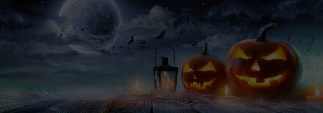 Jack-o-lanterns on a wooden surface with a lamp and candles backed by a cloudy moonlit sky with bats in the background