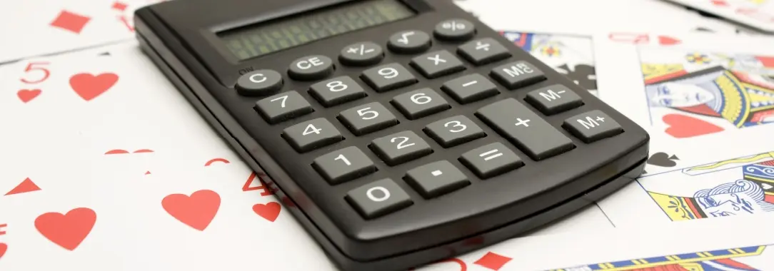 a small plastic pocket calculator on a table with playing cards all around to symbolize calculating poker math