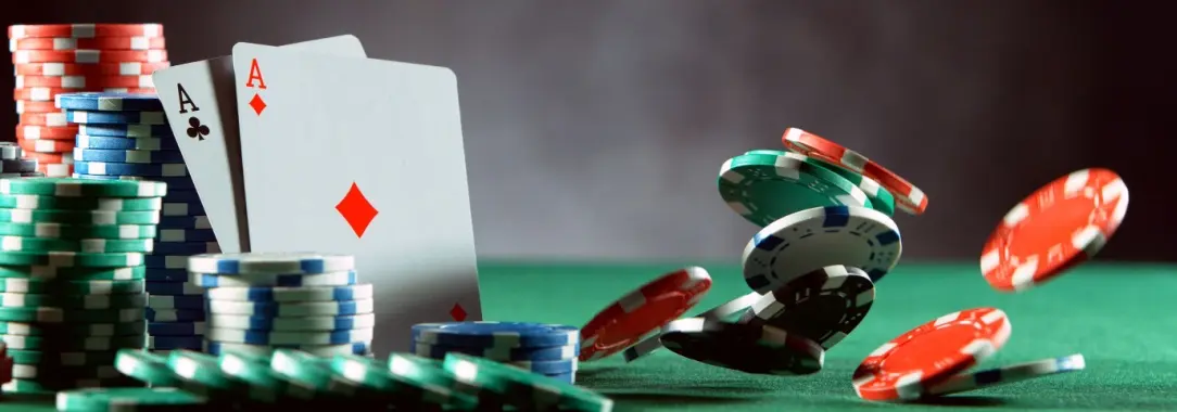 a poker table with gtreen, blue, and red chips stacked and a few chips falling onto the table. A pair of aces is shown.