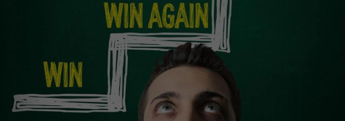 A photo of a man looking up with ‘Win’, ‘Win Again’, ‘Win More’ in a stepped format on green board on the wall behind him